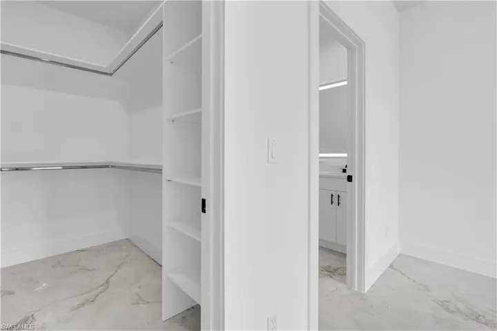 Walk-in closet featuring built-in shelving, chrome hanging rods, and large format marble-look tile flooring