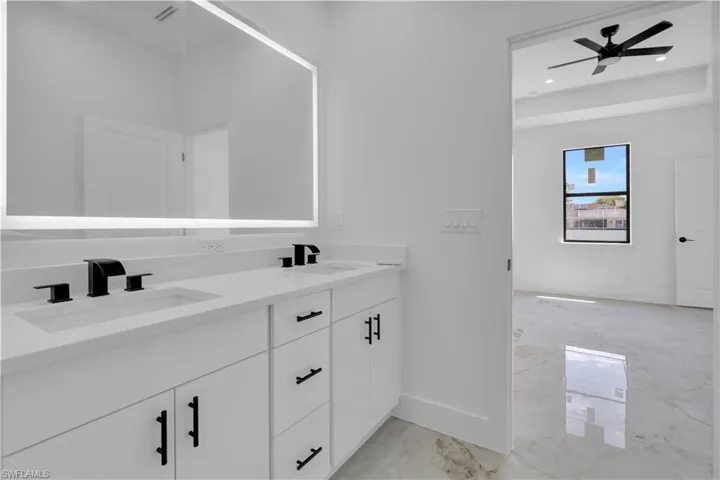 Dual vanity with white cabinetry, matte black hardware, and an illuminated mirror