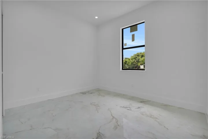 Spacious room featuring white walls, modern recessed lighting, a large window with black framing, and elegant marble-look flooring