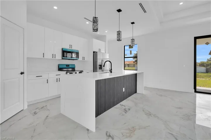 Modern kitchen featuring an extended island with a waterfall countertop and black fluted paneling