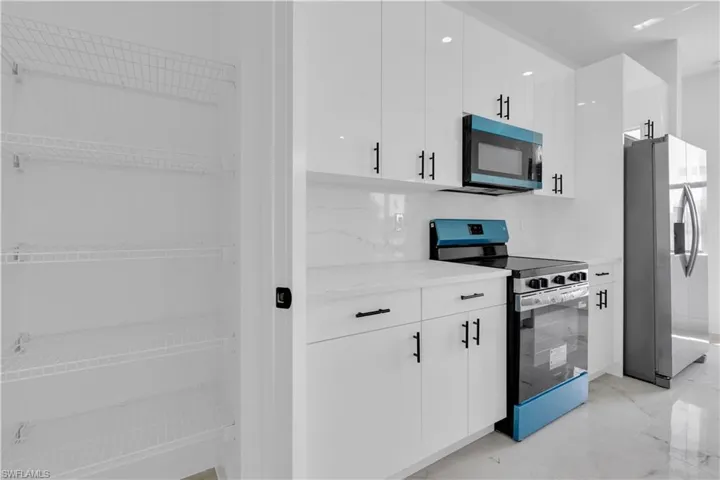 Contemporary kitchen featuring high-gloss white cabinetry with matte black hardware, a blue and stainless steel range, a matching blue microwave, and a side-by-side refrigerator