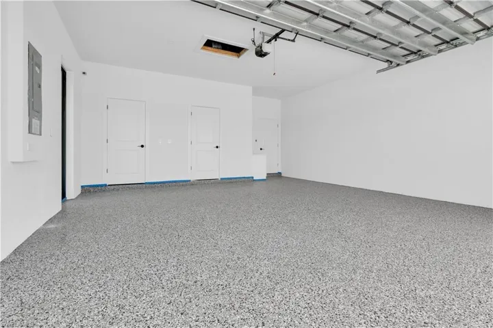 Spacious garage featuring a speckled epoxy floor, white painted walls, exposed ceiling joists, and multiple interior access doors