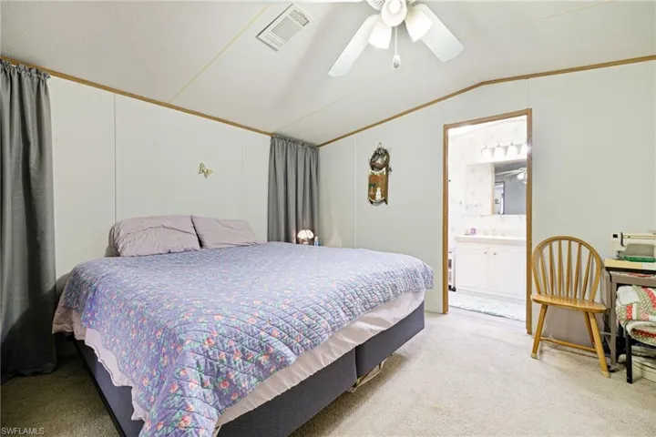 Bedroom with vaulted ceiling, light carpet, a sink, a ceiling fan, and ensuite bath
