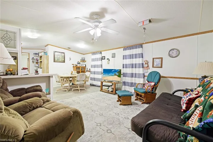 Living room with vaulted ceiling, a ceiling fan, wood finished floors, and ornamental molding