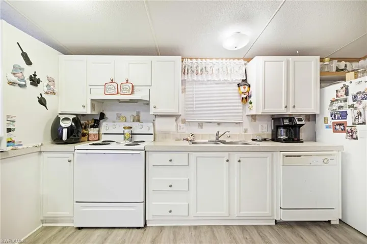Kitchen featuring white appliances, a sink, light wood-type flooring, white cabinets, and a textured ceiling