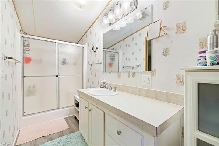 Full bath with vanity, wallpapered walls, a shower stall, and wood finished floors