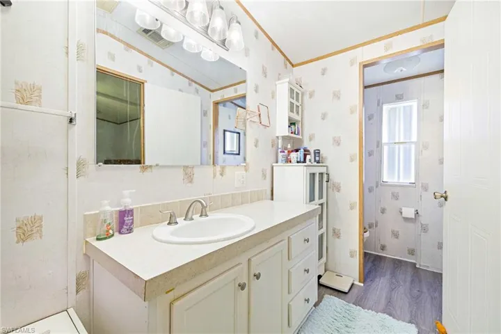 Bathroom featuring wood finished floors, wallpapered walls, crown molding, and vanity
