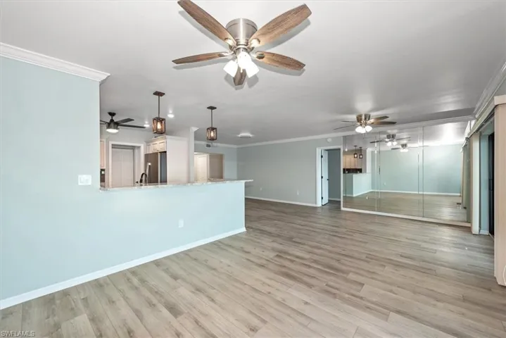 Unfurnished living room featuring ceiling fan, ornamental molding, and light wood-type flooring