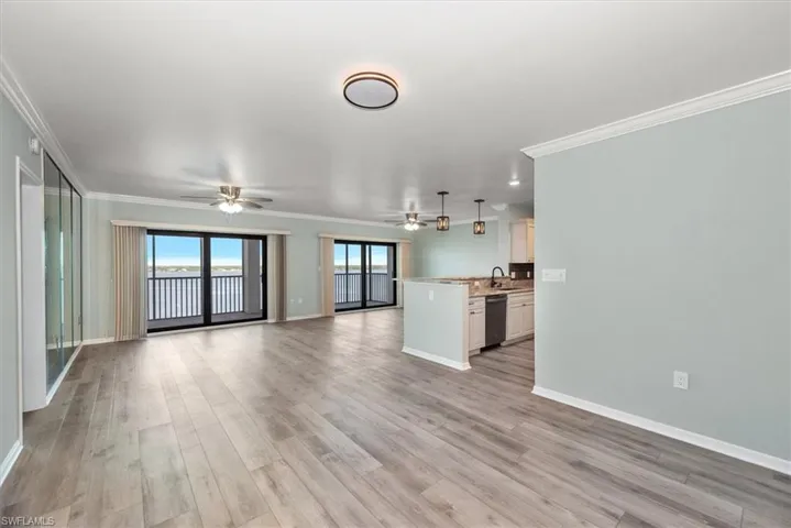 Unfurnished living room featuring a ceiling fan, ornamental molding, and light wood-type flooring