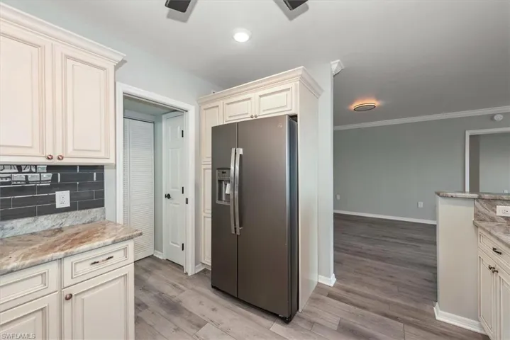 Kitchen featuring stainless steel fridge, decorative backsplash, light wood-style floors, ornamental molding, and light stone counters