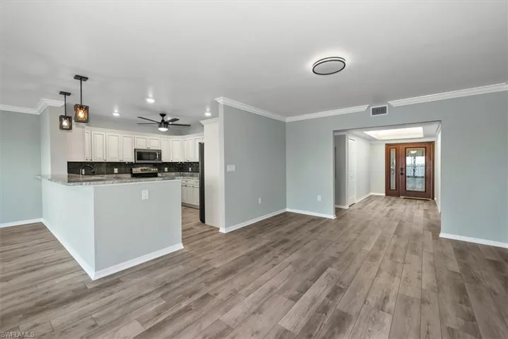 Kitchen with appliances with stainless steel finishes, ornamental molding, a peninsula, decorative backsplash, and white cabinets