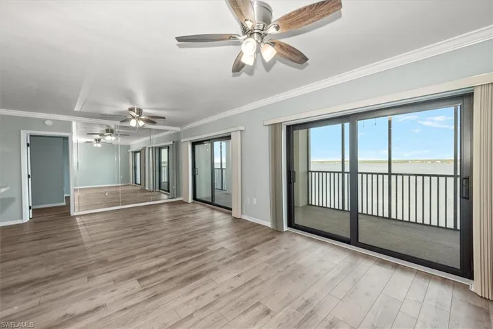 Unfurnished room with a ceiling fan, wood finished floors, a water view, and crown molding