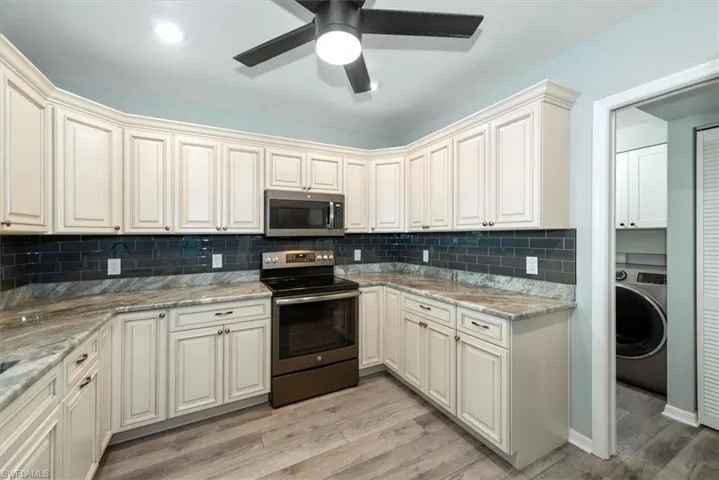 Kitchen featuring appliances with stainless steel finishes, washer / clothes dryer, tasteful backsplash, light wood finished floors, and ceiling fan