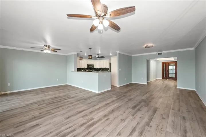 Unfurnished living room with ceiling fan, light wood-style floors, and crown molding