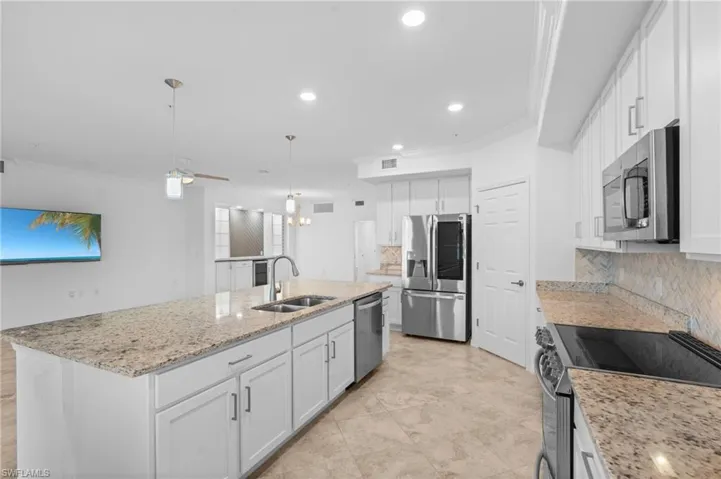 Kitchen featuring ornamental molding, a sink, an island with sink, white cabinets, and appliances with stainless steel finishes