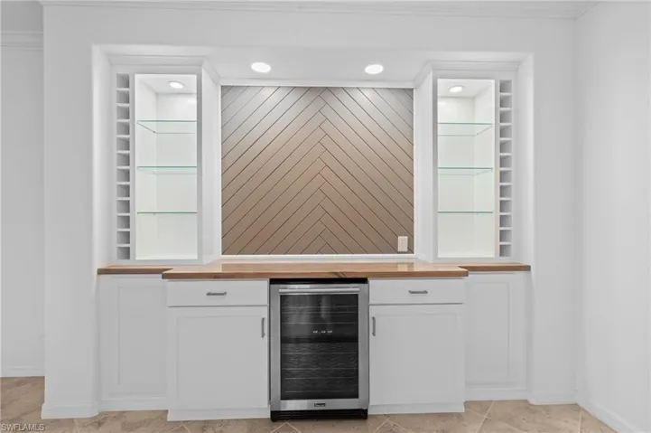 Bar featuring baseboards, beverage cooler, crown molding, and recessed lighting