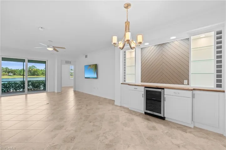 Kitchen with wine cooler, white cabinets, open floor plan, decorative light fixtures, and ornamental molding