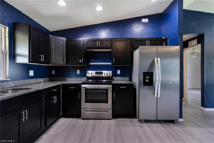 Kitchen featuring appliances with stainless steel finishes, lofted ceiling, dark stone countertops, light hardwood / wood-style floors, and sink
