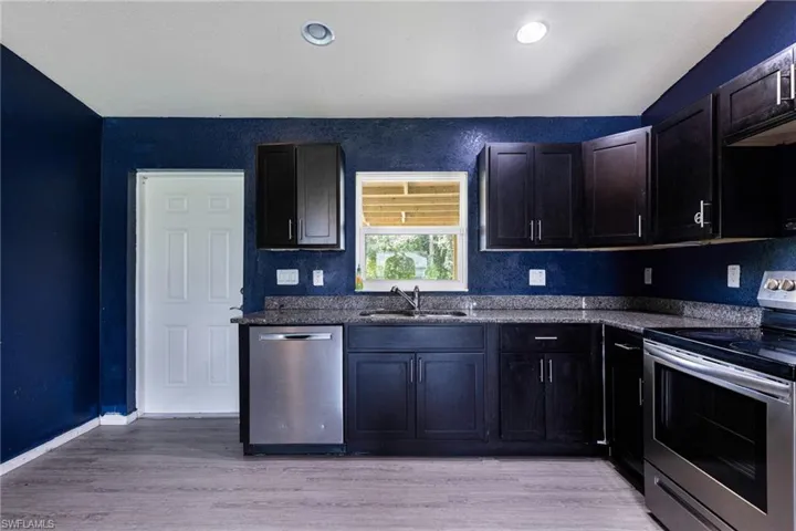 Kitchen with appliances with stainless steel finishes, sink, dark brown cabinets, and light hardwood / wood-style floors