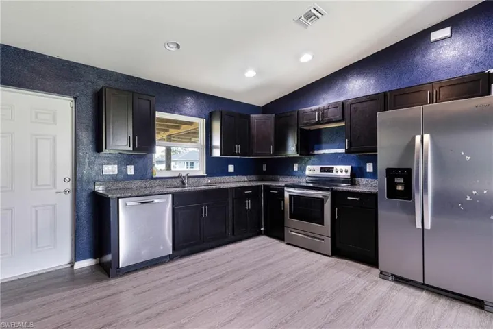 Kitchen featuring stainless steel appliances, vaulted ceiling, sink, tasteful backsplash, and light hardwood / wood-style floors