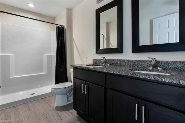 Bathroom featuring walk in shower, hardwood / wood-style flooring, dual vanity, and toilet