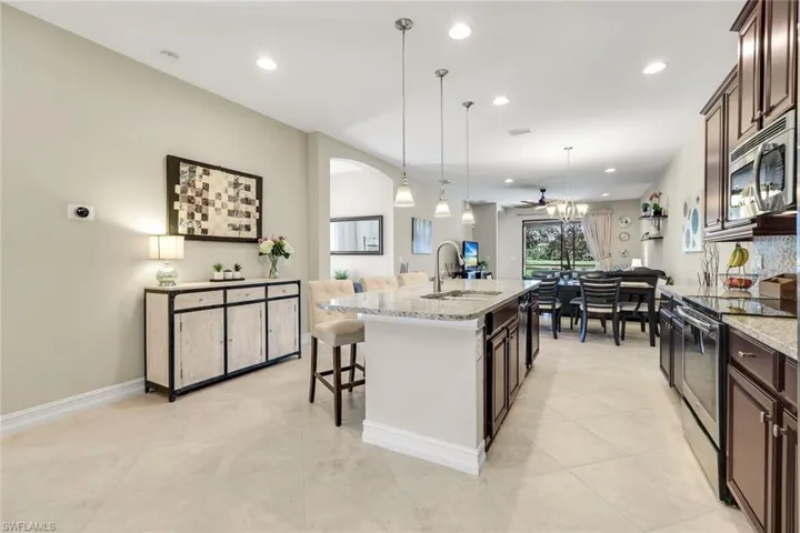Kitchen with stainless steel appliances, a breakfast bar area, hanging light fixtures, light stone counters, and recessed lighting