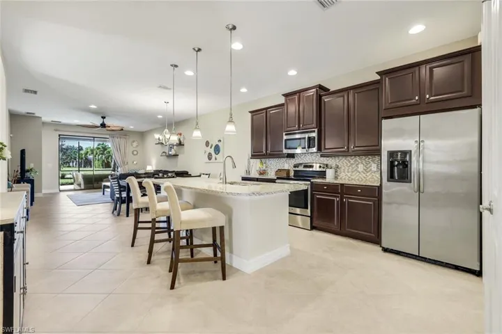 Kitchen featuring dark brown cabinetry, appliances with stainless steel finishes, open floor plan, a kitchen breakfast bar, and hanging light fixtures