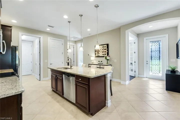 Kitchen featuring dark brown cabinets, light stone countertops, an island with sink, a breakfast bar, and stainless steel appliances