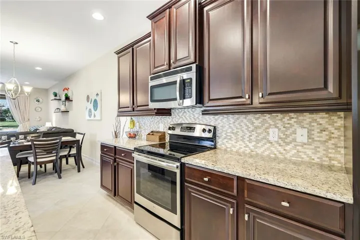 Kitchen with appliances with stainless steel finishes, light stone counters, pendant lighting, dark brown cabinets, and a chandelier