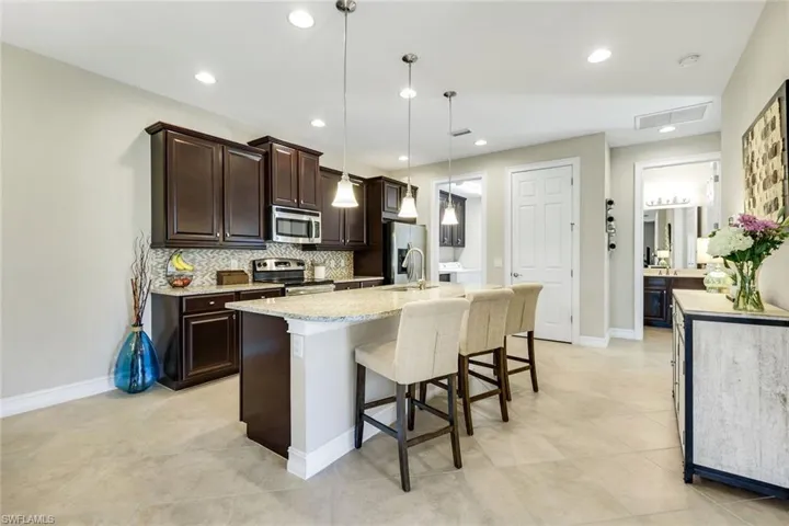 Kitchen with dark brown cabinets, a breakfast bar, light stone counters, stainless steel appliances, and a kitchen island with sink