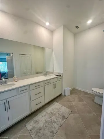 Bathroom featuring double vanity, toilet, tile patterned flooring, and baseboards