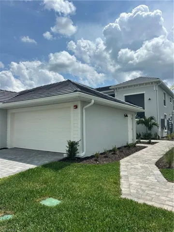 View of side of property featuring stucco siding, a yard, a garage, and decorative driveway