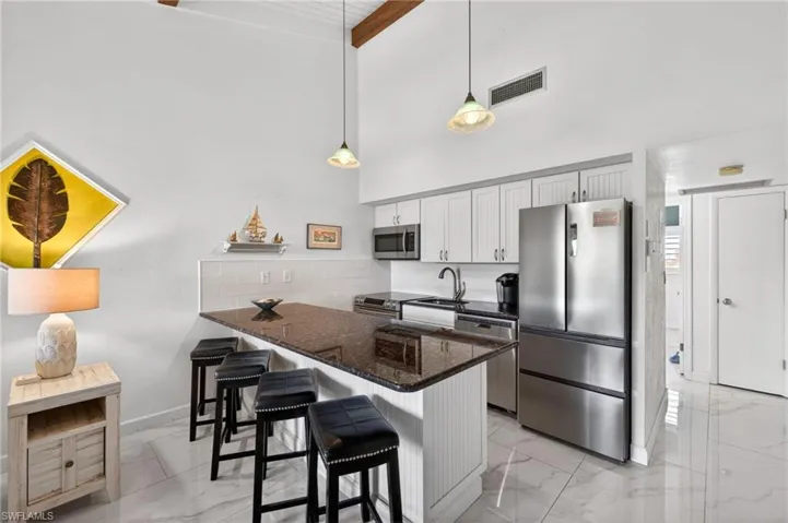 Kitchen featuring a breakfast bar with dark countertop, white shaker-style cabinetry, and stainless steel appliances