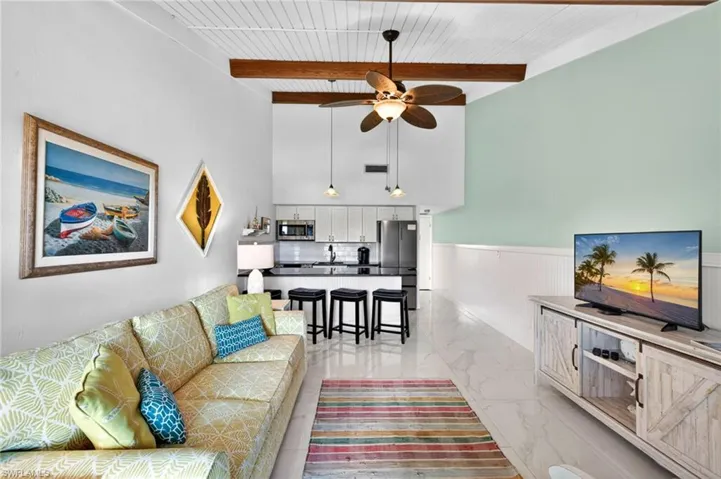 Open-concept living area with high vaulted ceilings, exposed wood beams, and a white plank ceiling