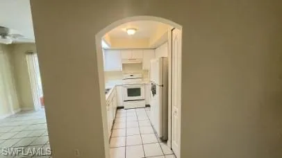 Kitchen with arched walkways, white appliances, white cabinets, and light countertops