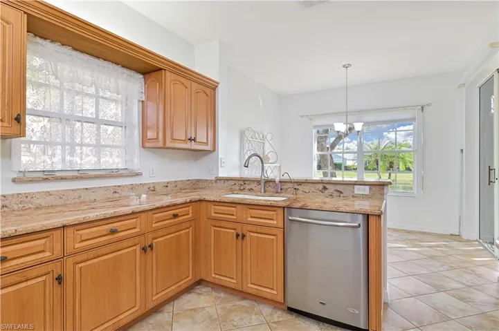 Kitchen featuring dishwasher, a chandelier, light stone countertops, a peninsula, and decorative light fixtures