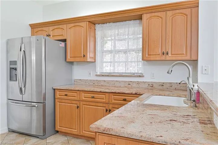 Kitchen with stainless steel fridge, light stone countertops, light brown cabinetry, and light tile patterned floors