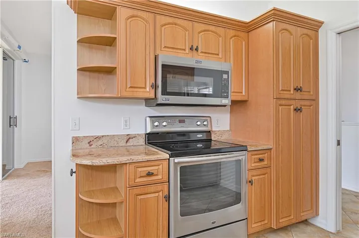 Kitchen with open shelves, stainless steel appliances, light stone counters, light brown cabinetry, and light colored carpet
