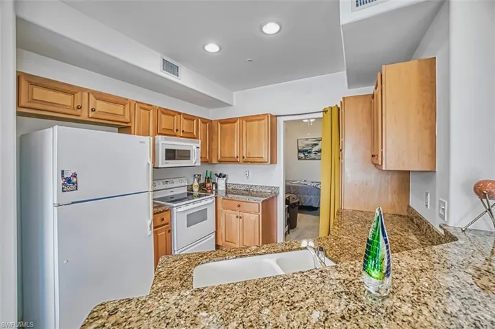 Kitchen with white appliances, light stone countertops, recessed lighting, and brown cabinets