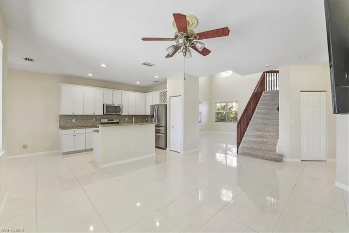 Kitchen with open floor plan, ceiling fan, a kitchen island with sink, white cabinetry, and stainless steel appliances
