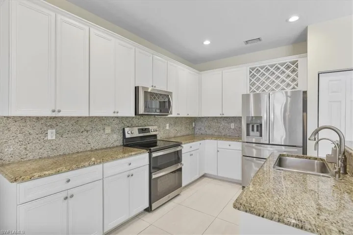 Kitchen featuring stainless steel appliances, white cabinetry, light stone countertops, and recessed lighting