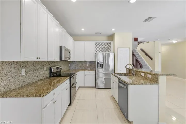 Kitchen with stainless steel appliances, dark stone counters, white cabinetry, a kitchen island with sink, and light tile patterned flooring