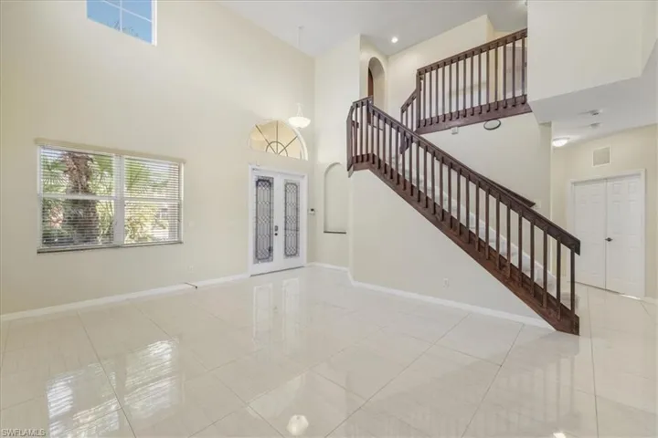 Unfurnished living room with french doors, a high ceiling, light tile patterned flooring, and arched walkways