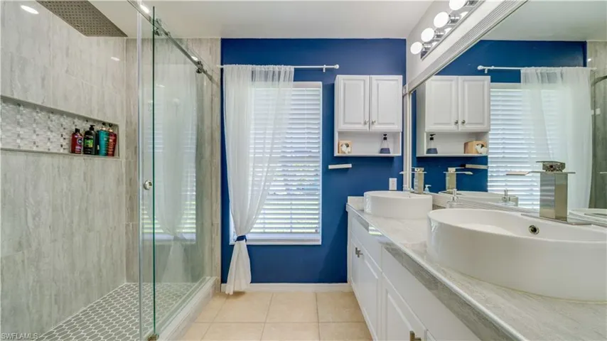 Bathroom with light tile patterned flooring, double vanity, and a shower stall