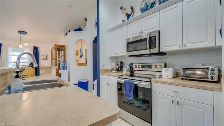 Kitchen with stainless steel appliances, white cabinetry, decorative backsplash, and light countertops