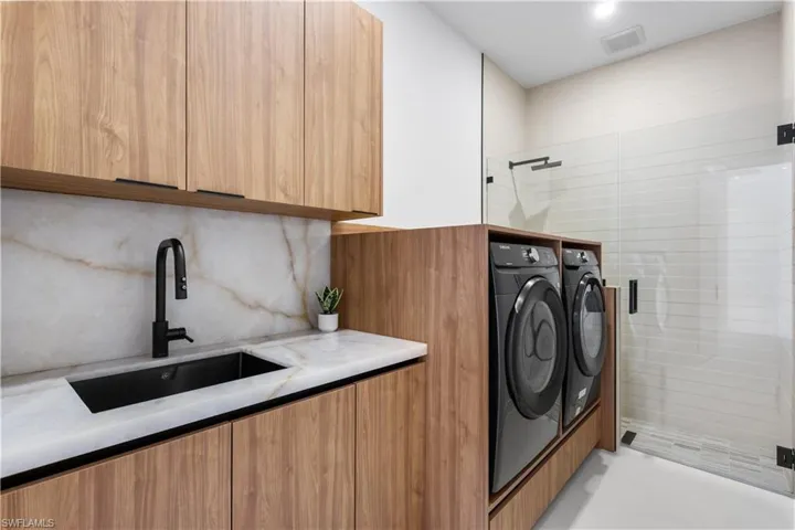 LAUNDRY is CONCEALED by ACOUSTIC PANELING door & in the entrance hallway & features CLEANING STATION for YOU & FURRY COMPANIONS, SAMSUNG washer & dryer, laundry tub w/ full backsplash & storage cabinets.