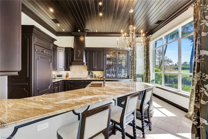 Kitchen featuring a breakfast bar, backsplash, dark wood finish cabinets, a chandelier, and wooden ceiling