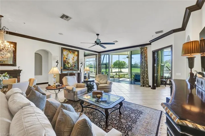 Living room with arched walkways, a ceiling fan, crown molding, light tile patterned floors, and hanging lights
