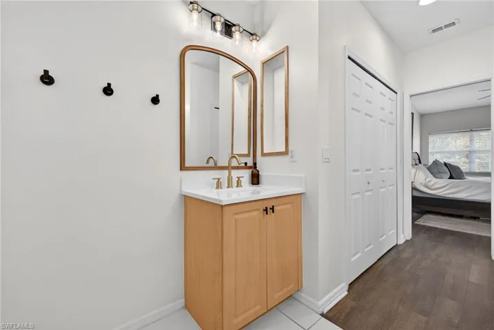 Primary Bathroom with morden vanity featuring a light wood-finish cabinet with black hardware, a white countertop, and a gold-finish faucet