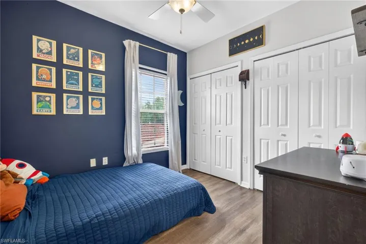 Bedroom featuring wood-finish flooring, a window with blinds, and two white bi-fold closet doors